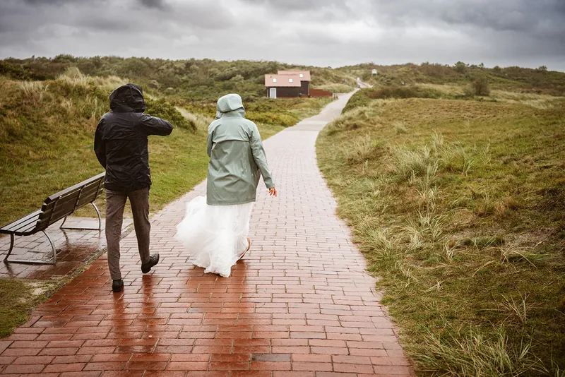 Paar spaziert trotz Regen und Wind über den Dünenweg