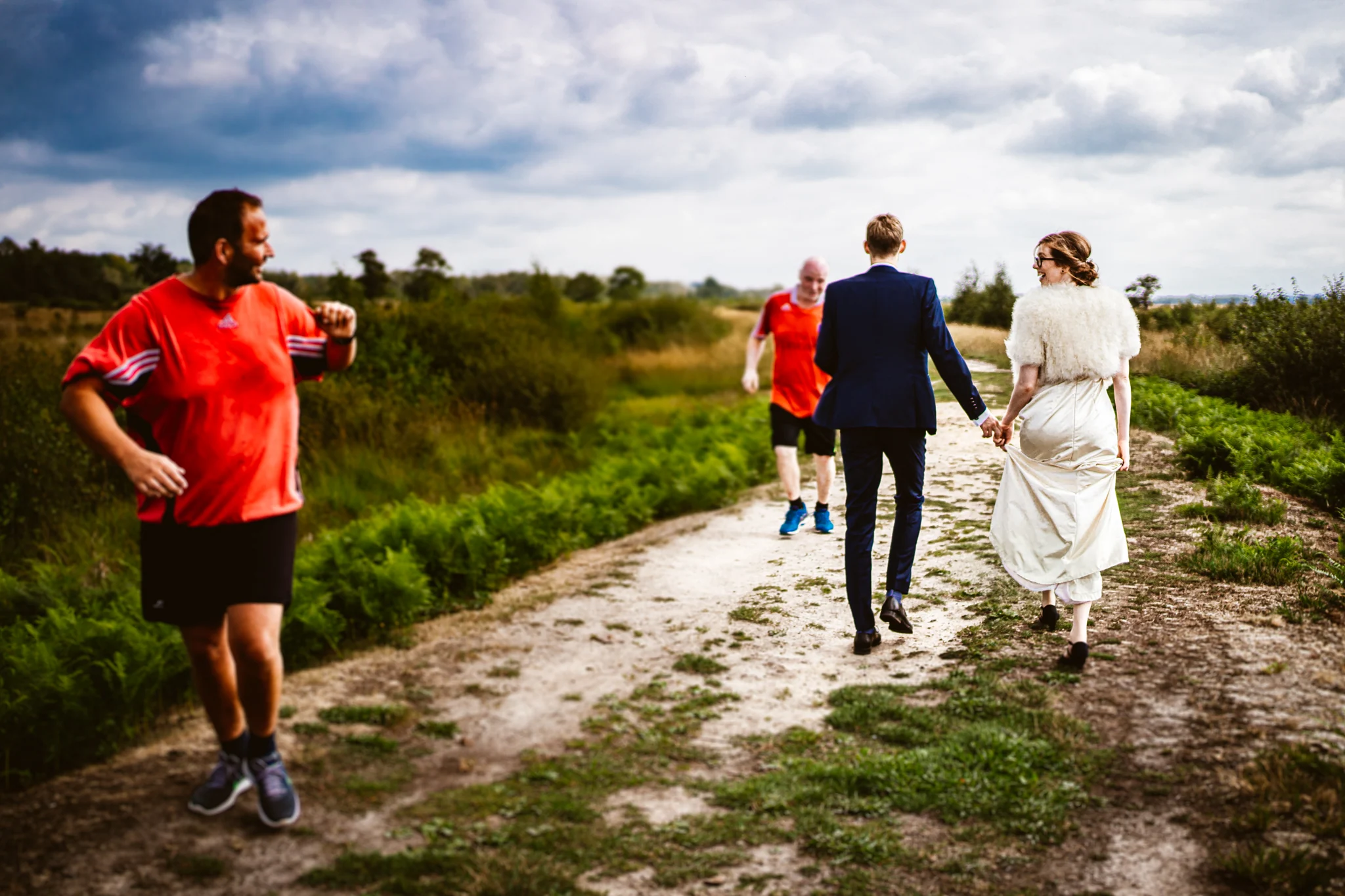 Hochzeitspaar und Gäste laufen gemeinsam über einen Schotterweg