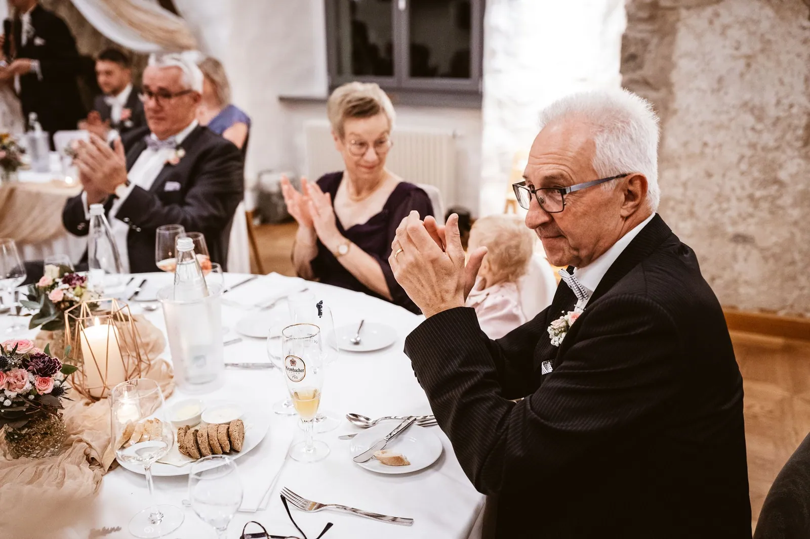 Gäste sitzen gemeinsam an einem gedeckten Hochzeitstisch