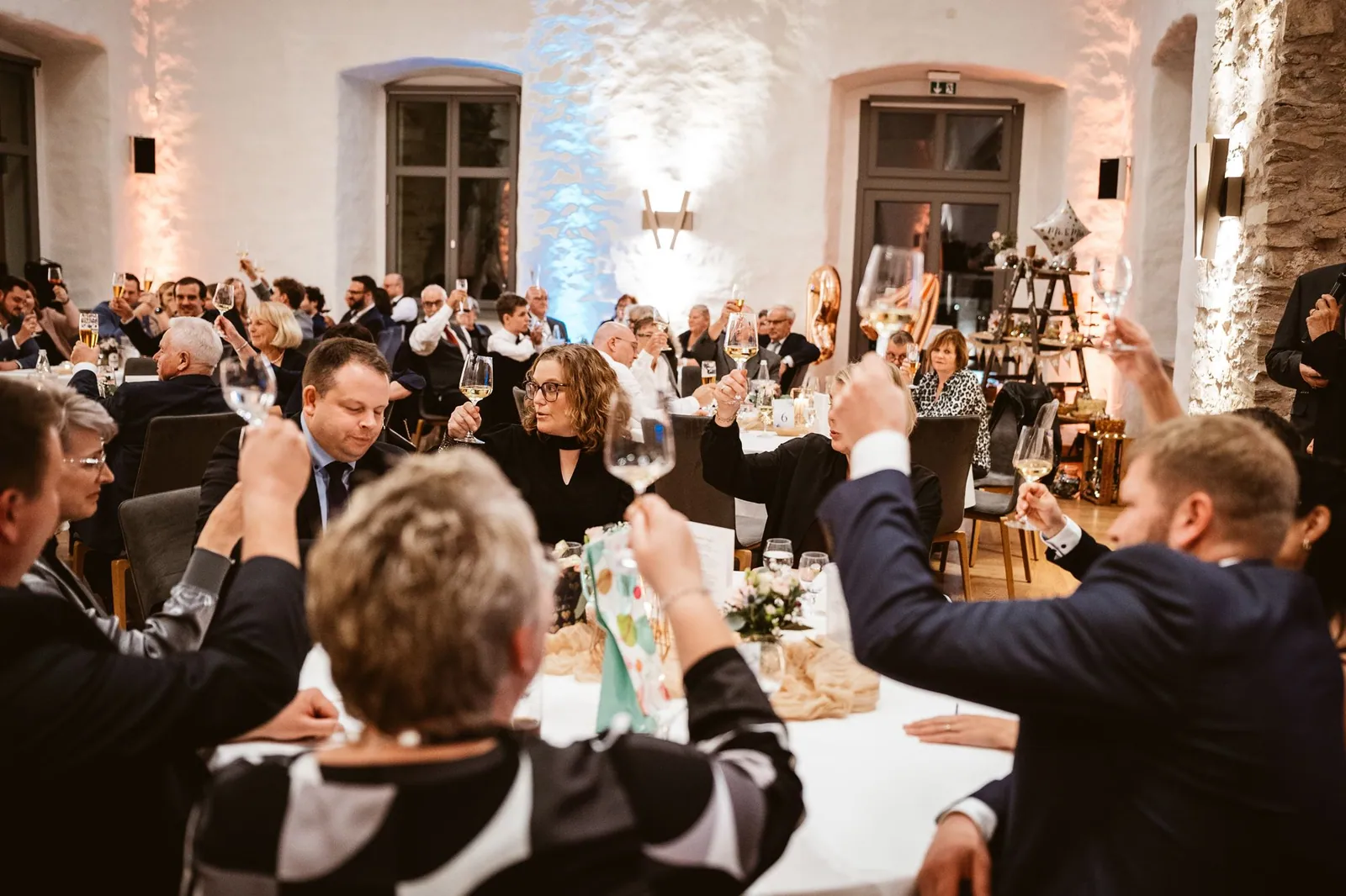 Gäste heben ihre Gläser an den Hochzeitstischen