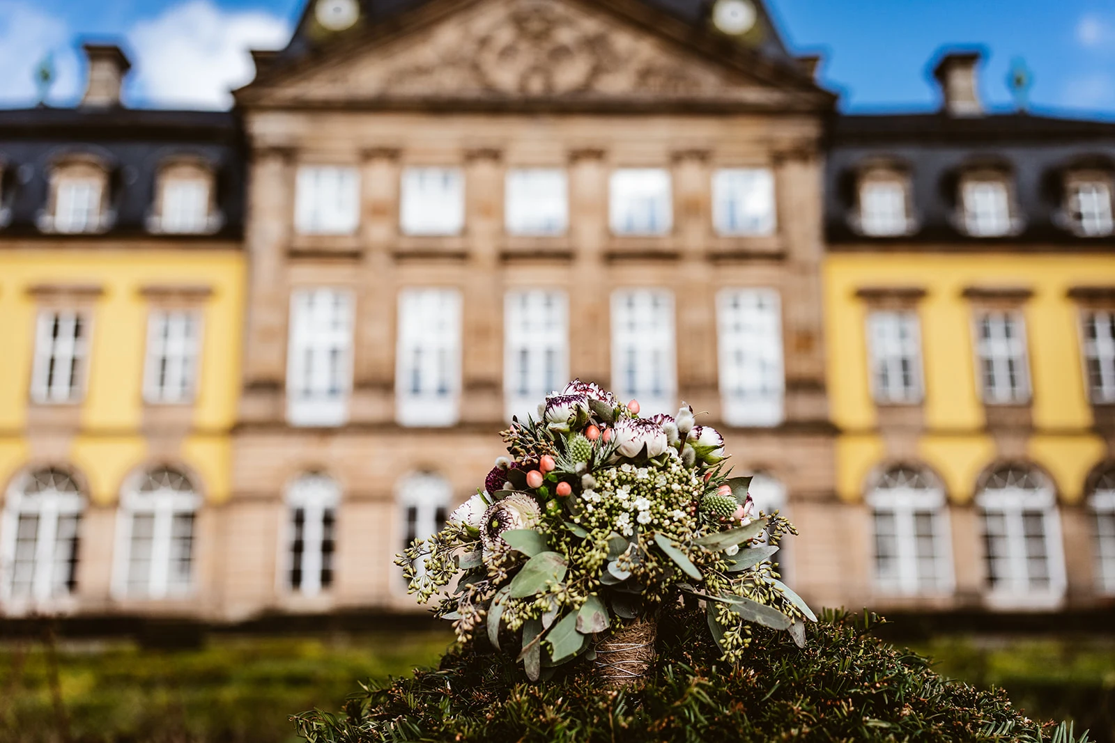 Brautstrauß und Schlossfassade im Sonnenschein